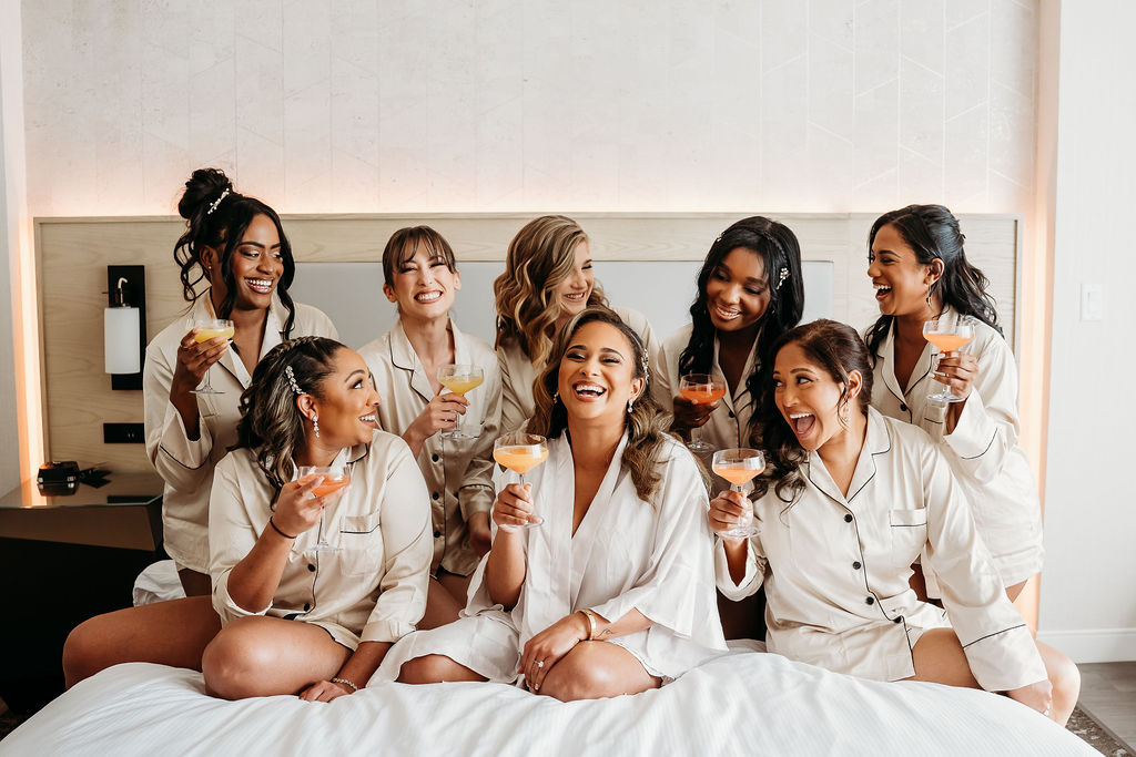 bride getting ready, bride and bridesmaid on bed drinking cocktail, beige silk pajamas, arizona wedding photographer, The Westin Tempe