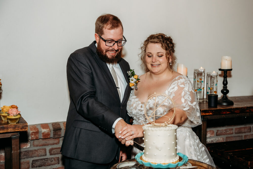 Bride and groom cutting the cake, cake is one tier with pearl dots with a simple wooden initial cake toppper