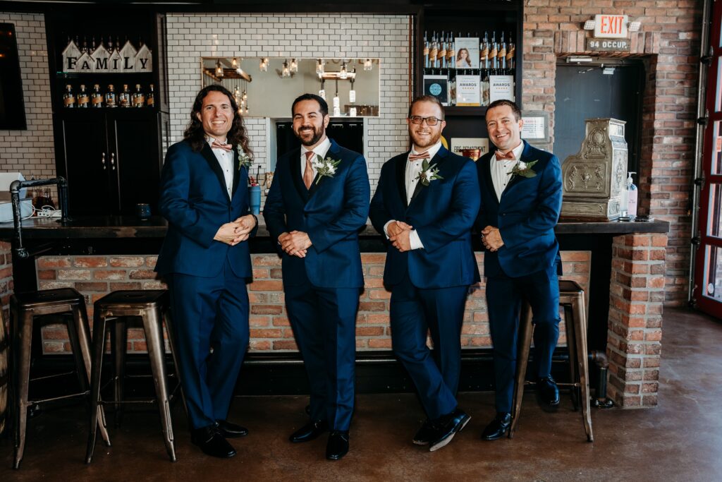 groom and groomsmen in navy blue tux standing at bar at the fire house event center
