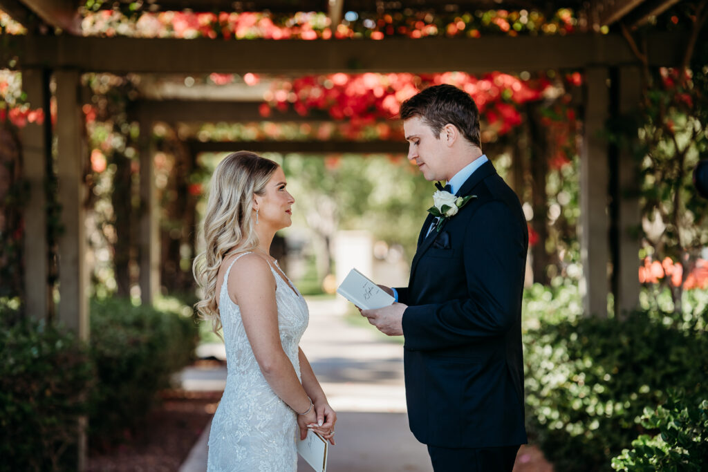 First look of couple reading vows, bride and groom under veranda with bougainvillea 
