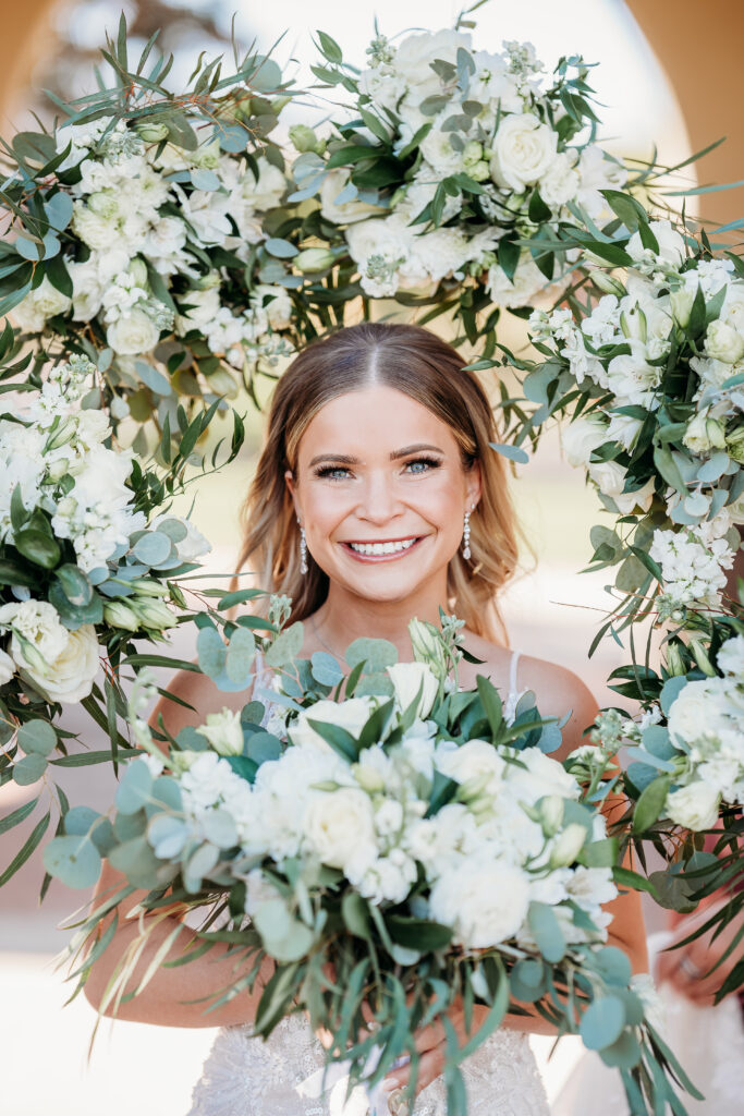 Bride Posing Ideas, bride with bouquet wreath around her, bride with slick back hair and drop earrings, white floral wedding bouquet, arizona wedding photographer