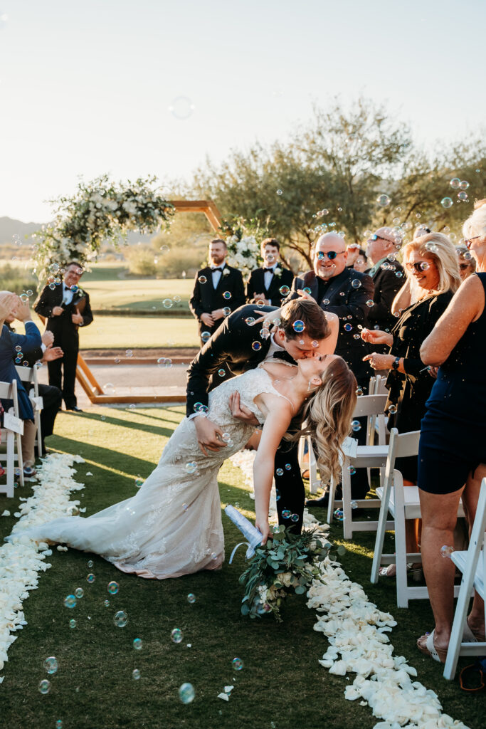 Groom kissing the bride at the end of the aisle at verrado golf club wedding ceremony, arizona wedding photographer, hexagon wood arch with white florals